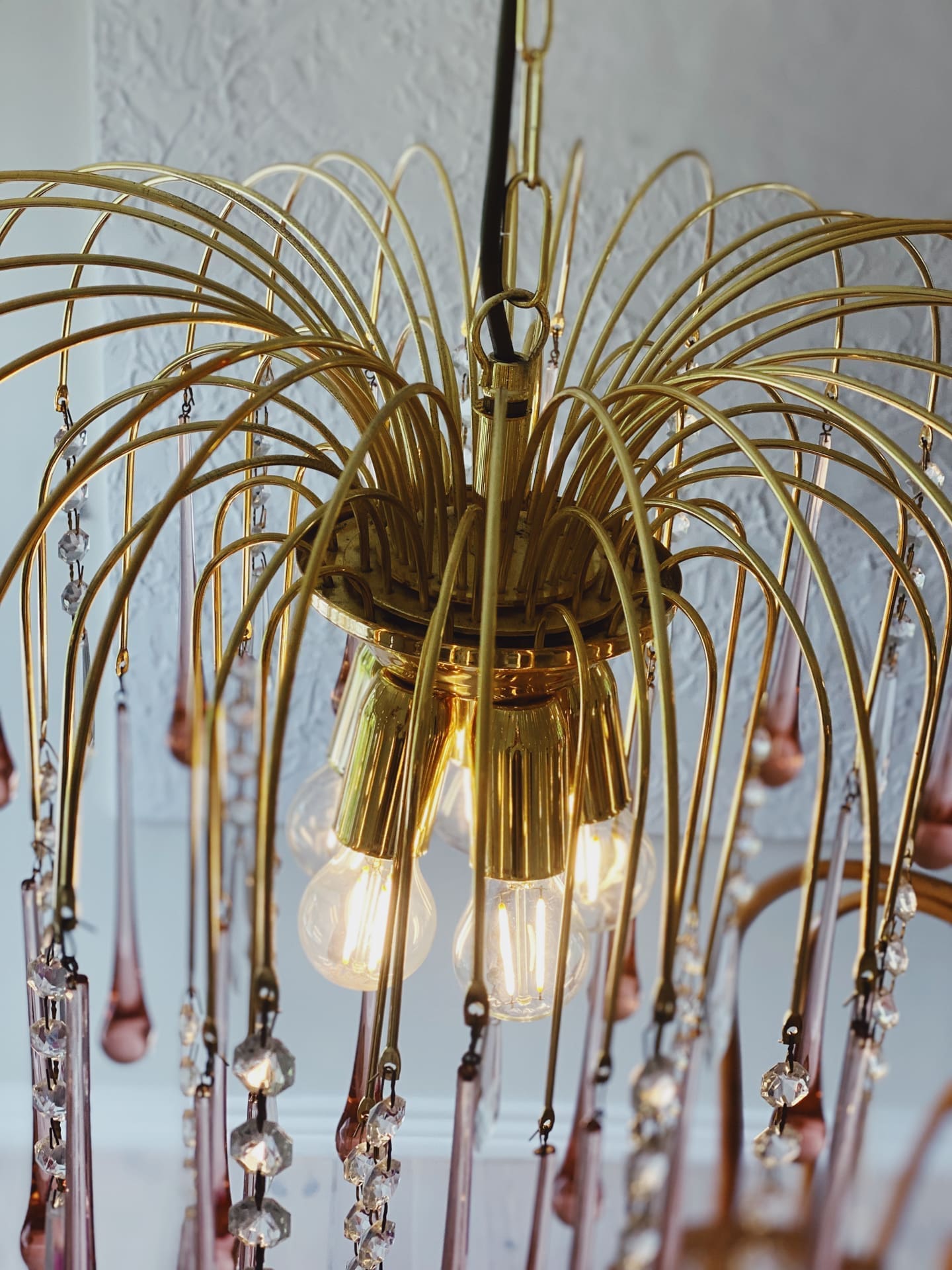 Gold chandelier with hanging crystals against a white wall